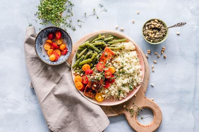 Food is served on top of a white cloth with a tan linen napkin next to it. The food is rice, sliced carrots, and green beans, with other unknown items in it.